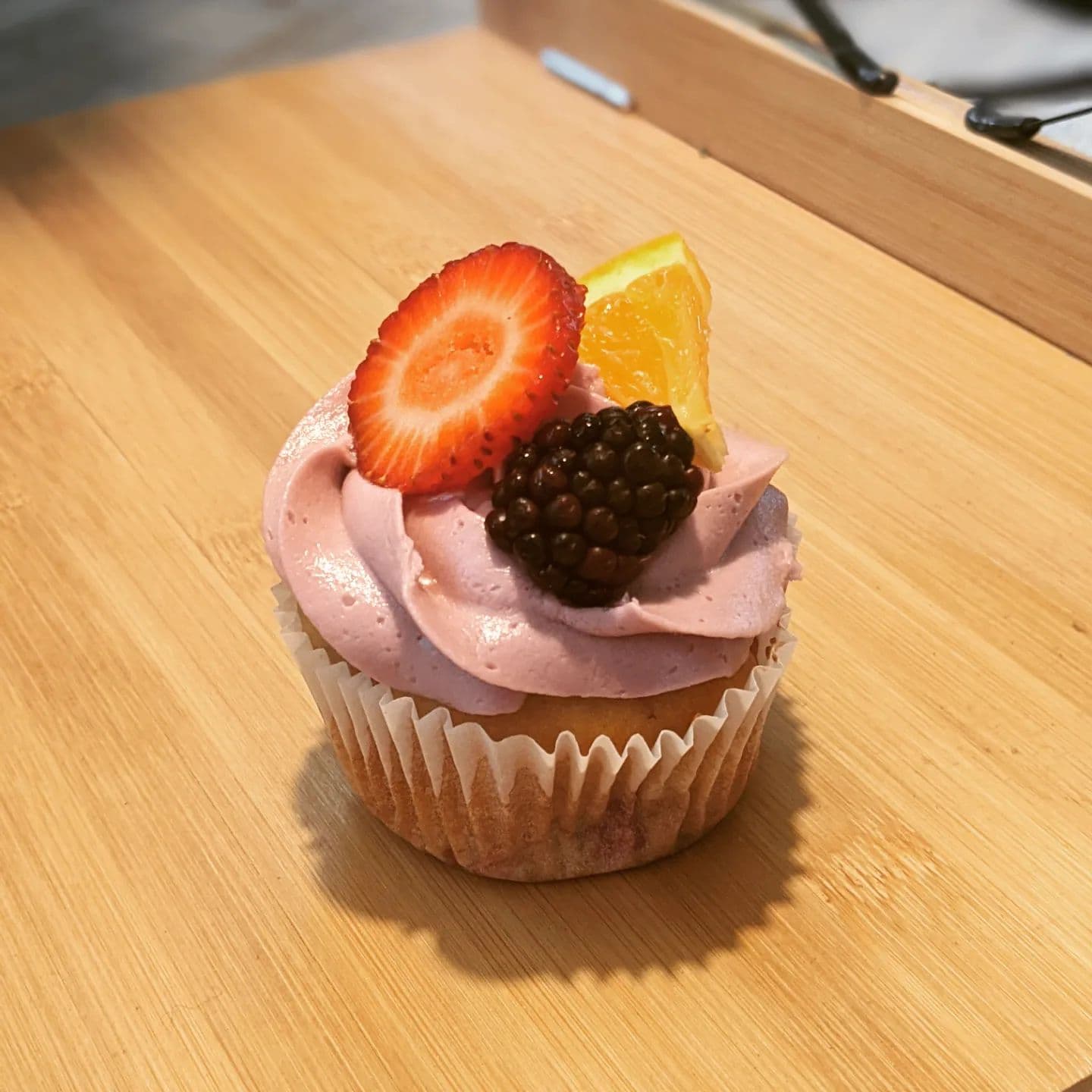 Pink frosted cupcake topped with a strawberry slice, a blackberry, and an orange wedge.